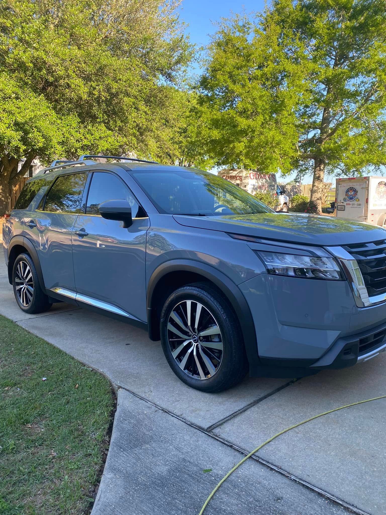 Gray SUV parked in a driveway under leafy trees on a sunny day