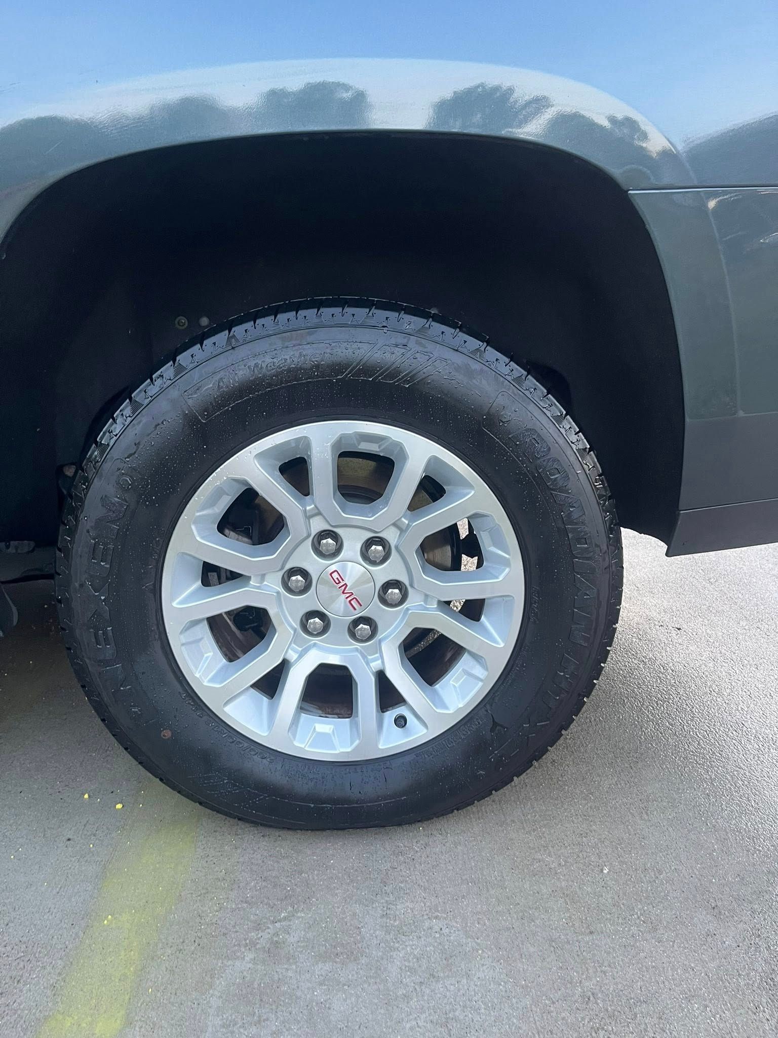 Close-up of a black SUV’s front wheel and silver alloy rim on a sunny road.