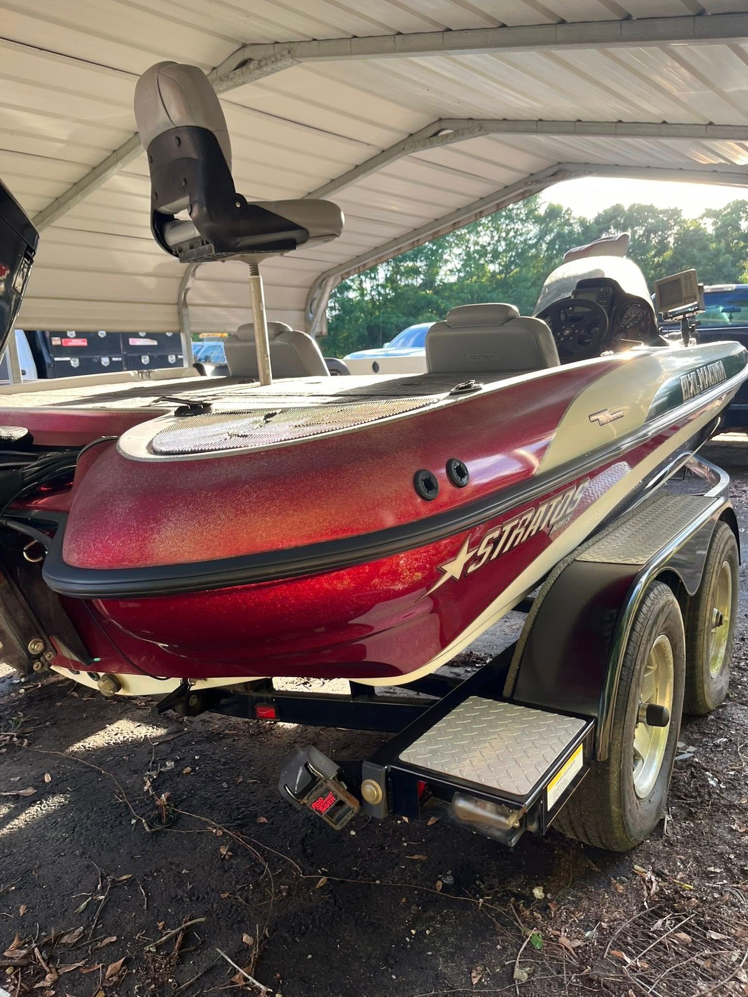 Red bass boat on a trailer under a carport, with a pedestal seat and black trim.