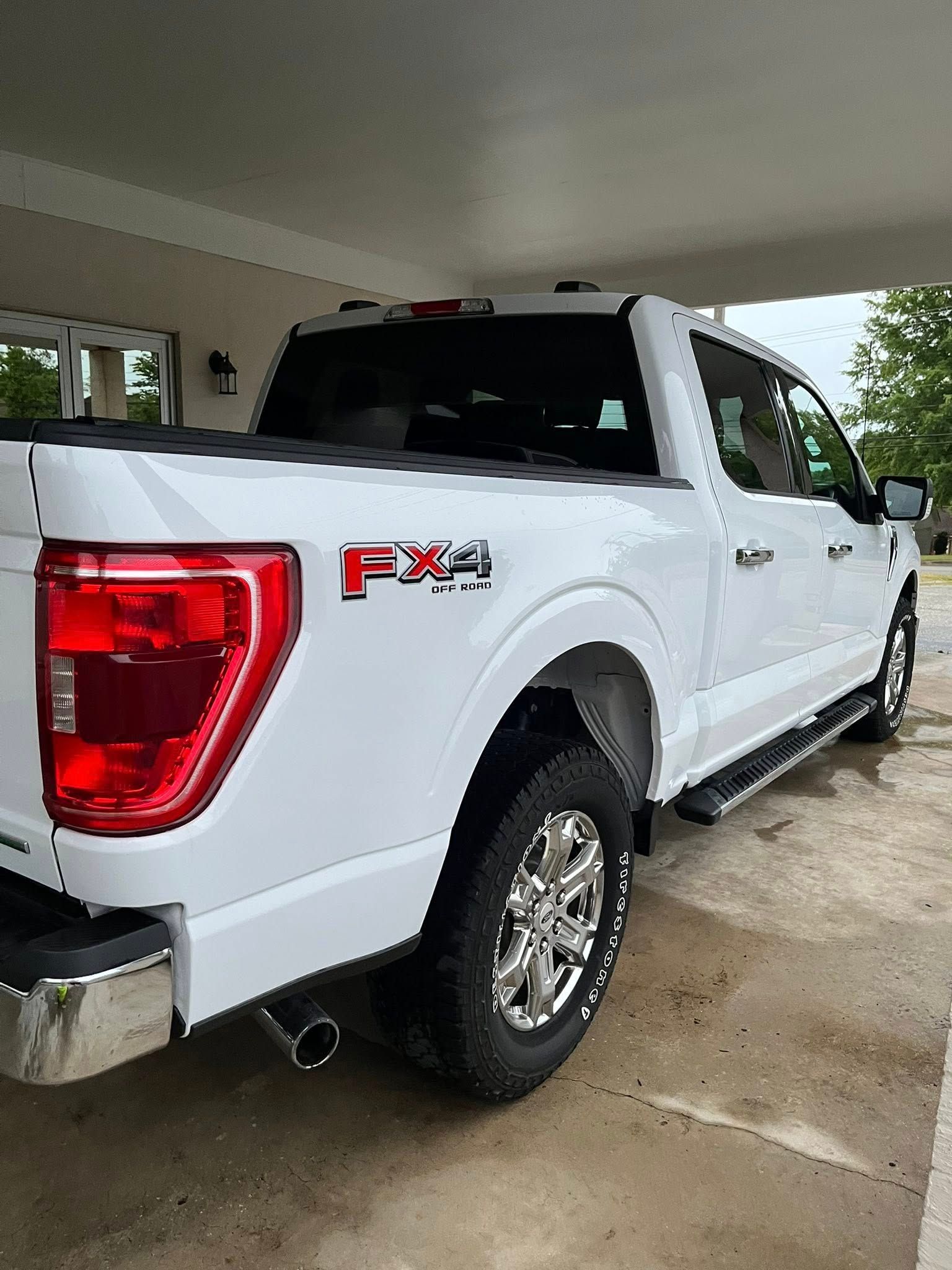 White Ford F-150 FX4 pickup parked under a carport on a wet driveway