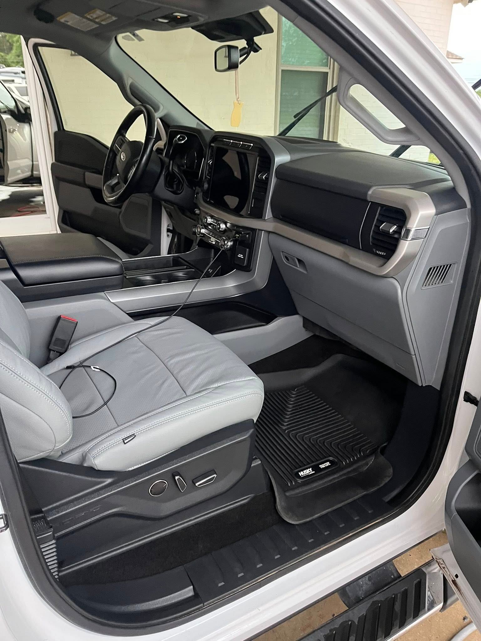Luxury car interior with grey seats and doors open, showing dashboard and front cabin from the passenger side