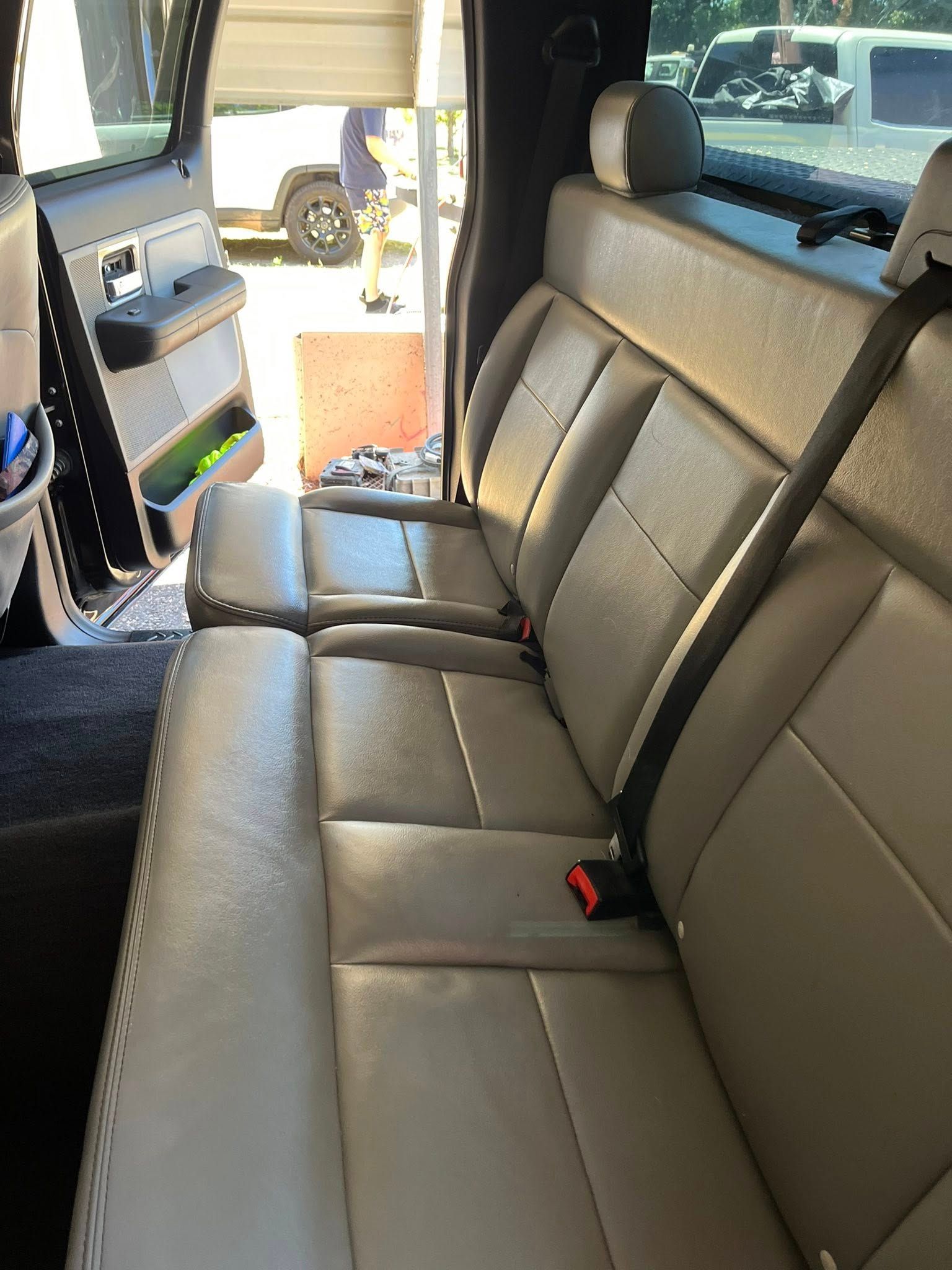 Gray leather back seat inside a vehicle, with center armrest and side window visible.