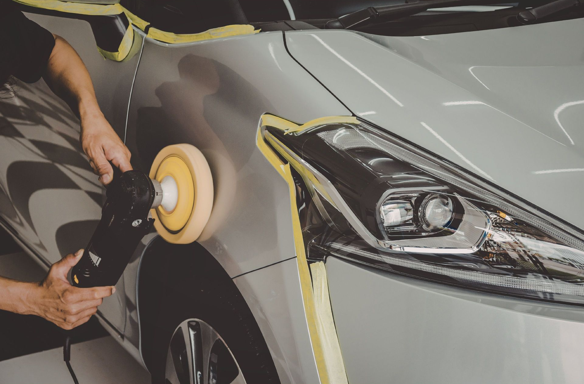 Worker in orange gloves spray-painting a car panel in a paint booth