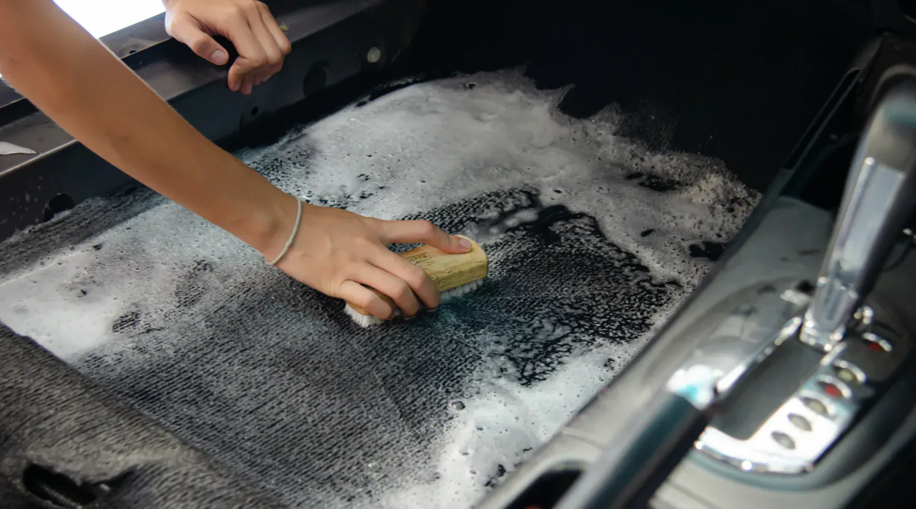 Hands scrubbing a sudsy black sink with a sponge beside a stainless steel faucet.