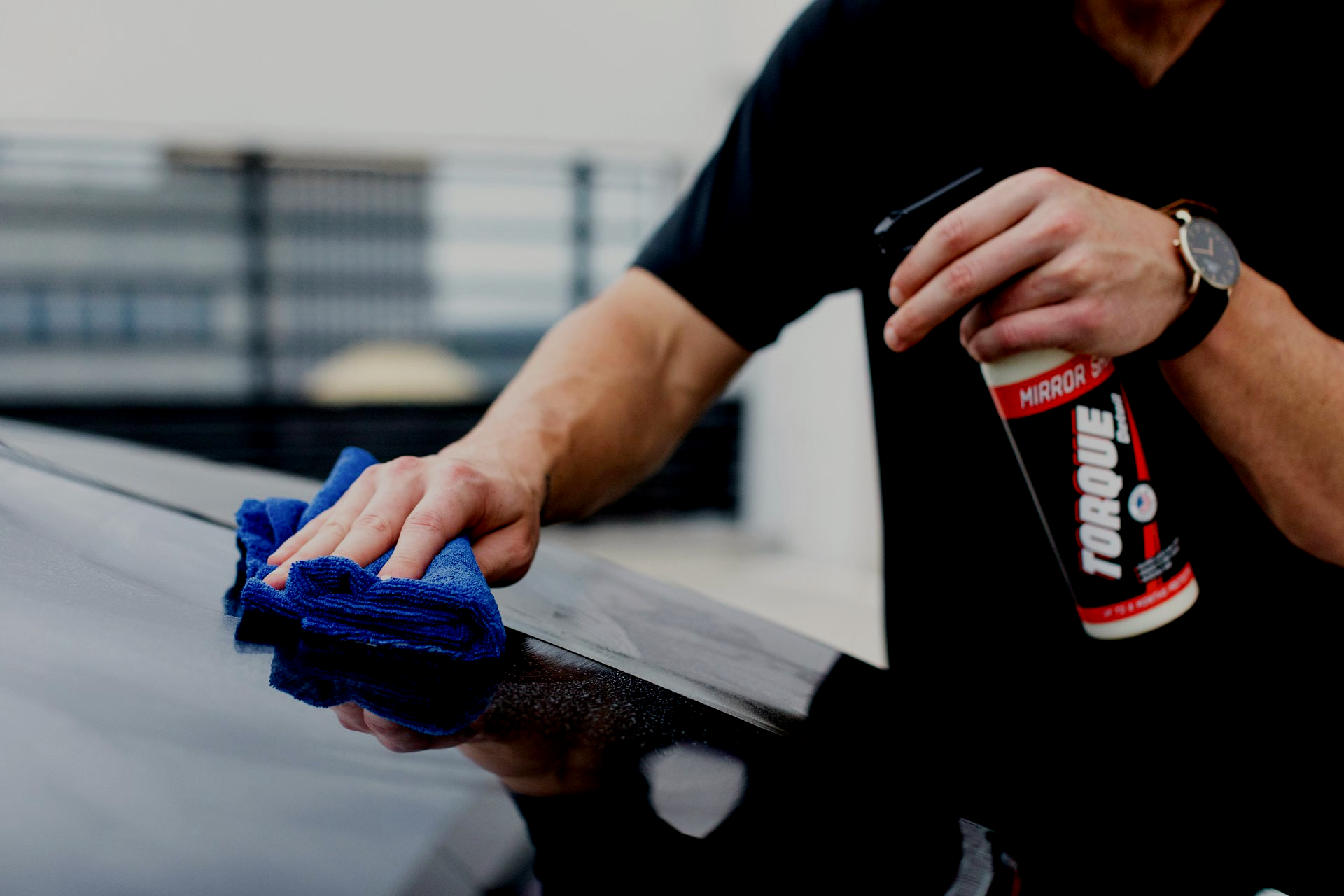 Person polishing a white car’s front fender with a buffer, masking tape around the headlight and body edges