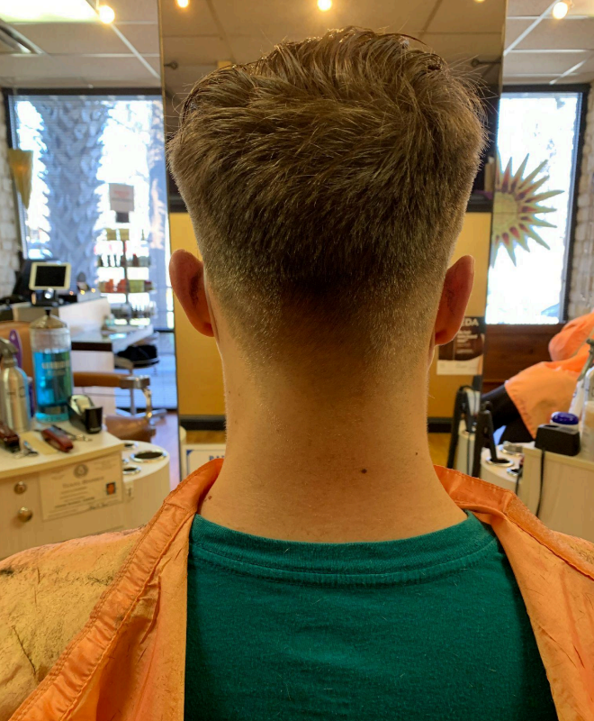 Barber trimming a man’s hair with clippers in a dimly lit barbershop.