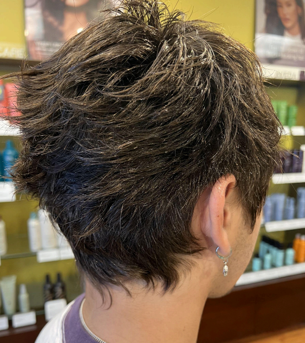 Person getting a haircut, seen from behind, with clippers trimming the back of the head.