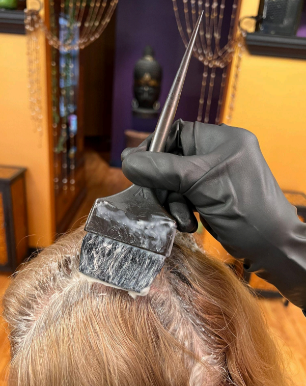 Hairdresser applying dye to a client’s wet hair with a brush and gloves in a salon.