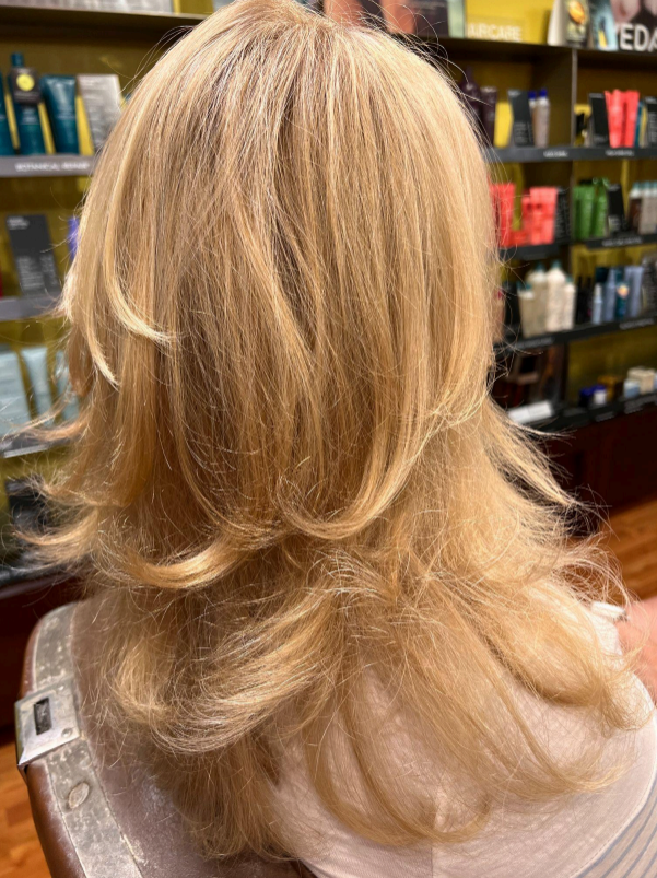 Hairdresser applying dye to a client’s wet hair with a brush and gloves in a salon.