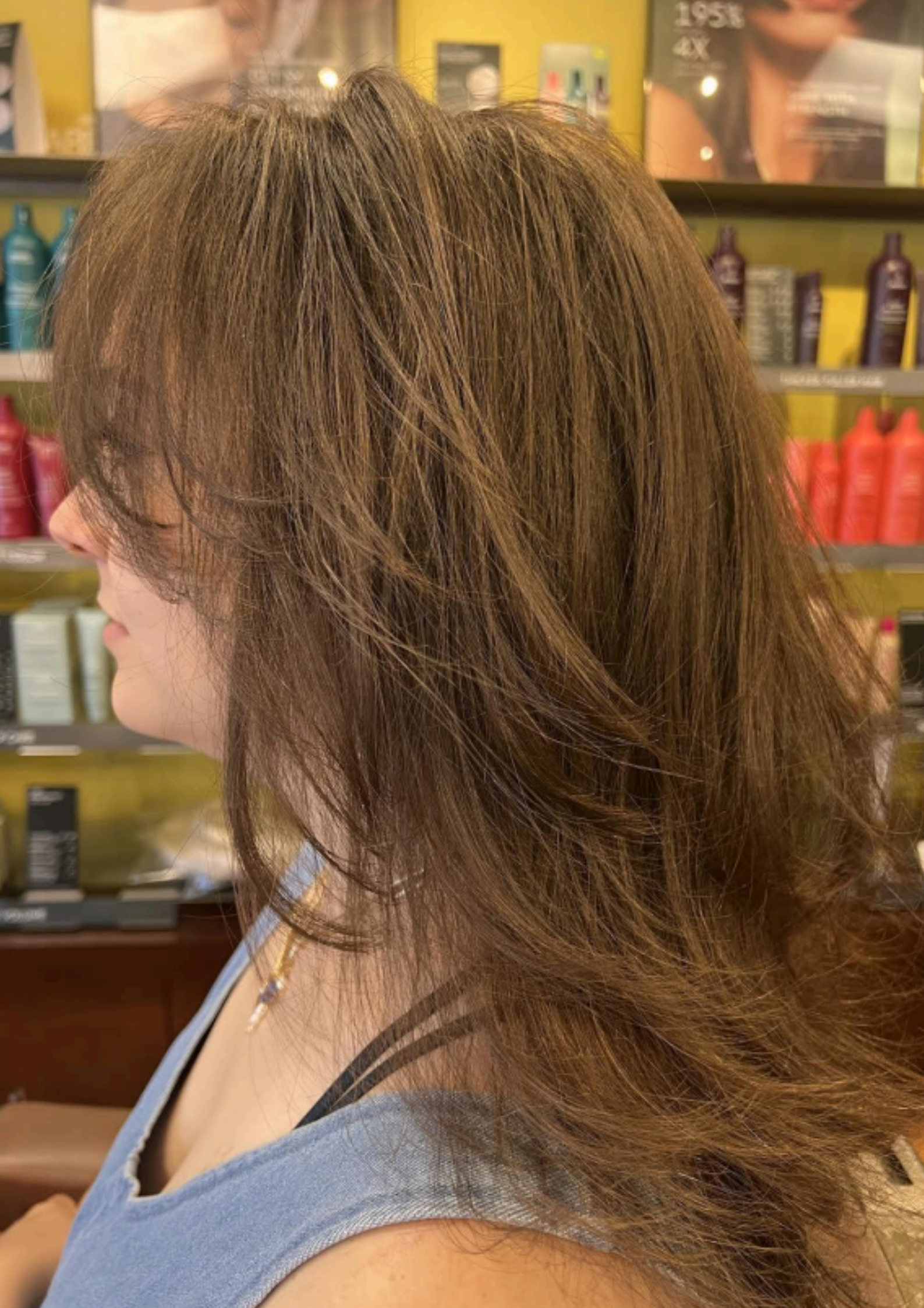 Woman with highlighted brown hair in a yellow patterned top, seated in a salon with blurred background