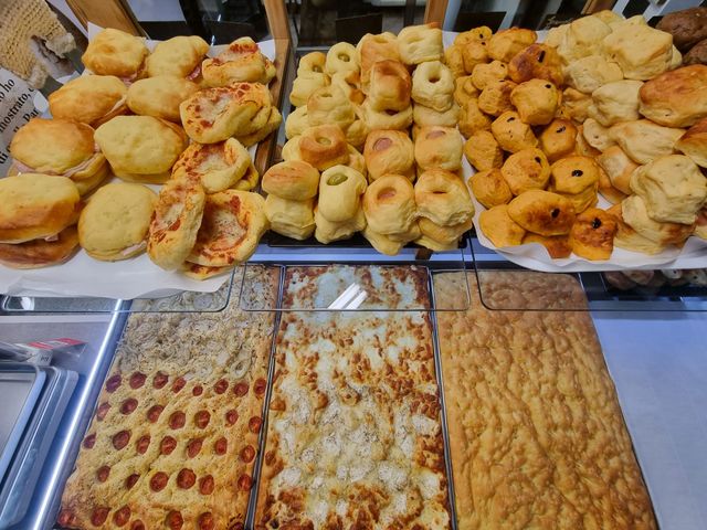 Esposizione di prodotti da forno: vari prodotti da forno, tra cui focacce, panini e prodotti salati.