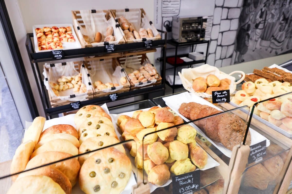 Esposizione di prodotti da forno con vari tipi di pane, panini e pasticcini esposti in cestini e dietro vetrine.