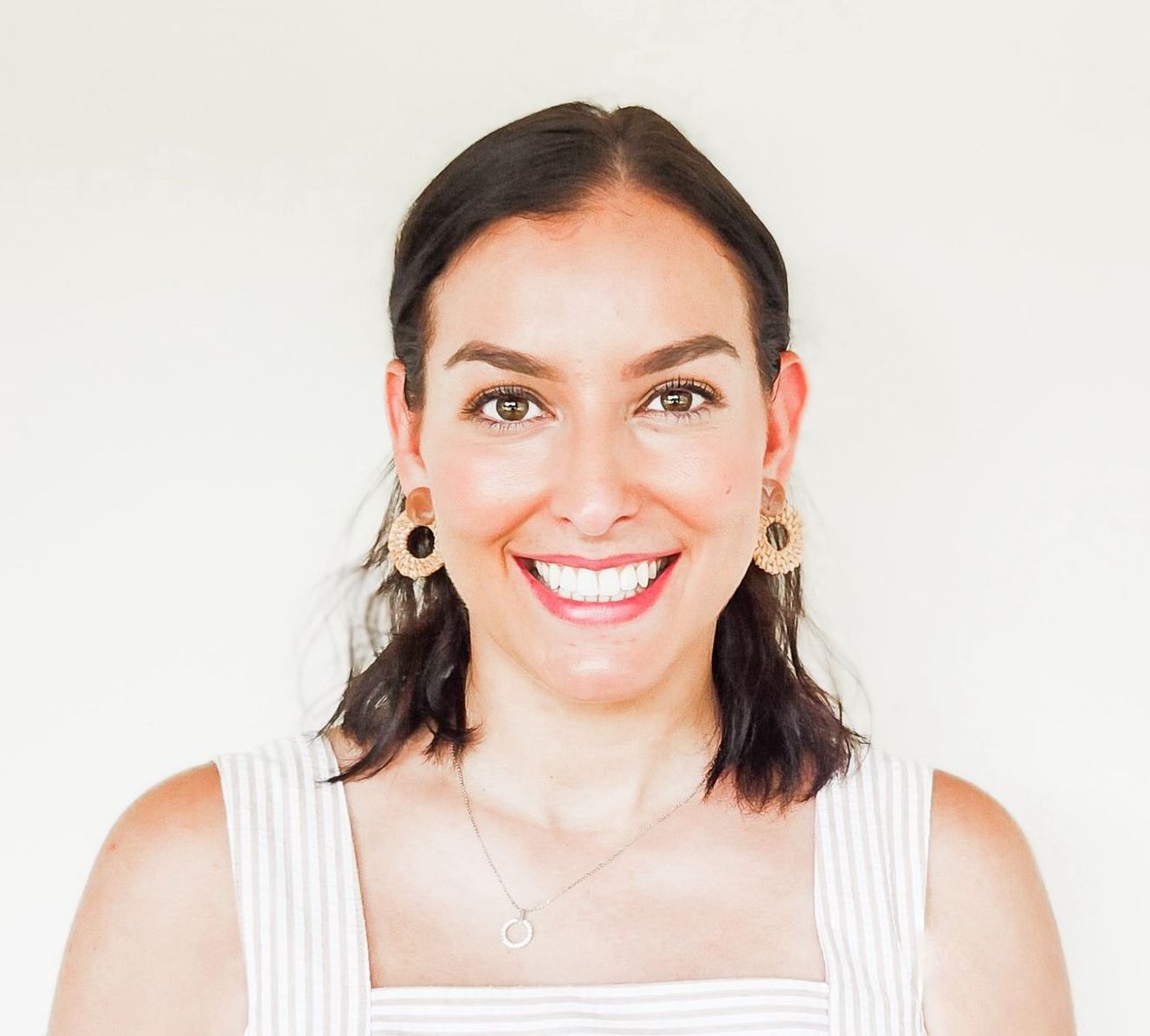 Smiling woman with dark hair in a white top against a plain light background