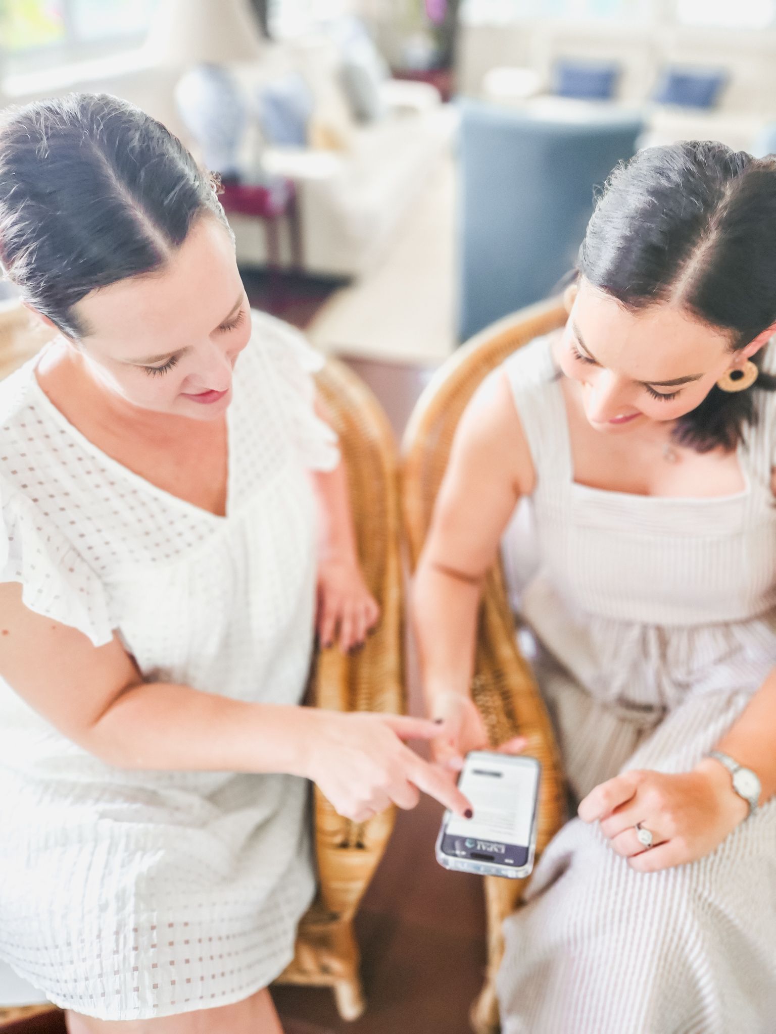 Two women in white dresses looking at a smartphone together in a bright room