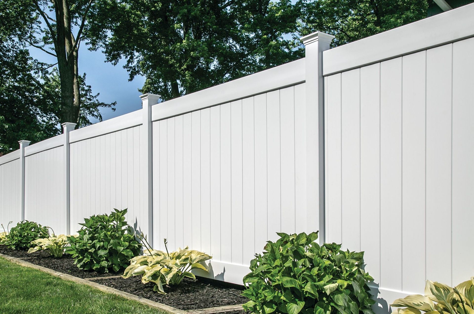 A wooden fence surrounds a lush green lawn in a backyard.