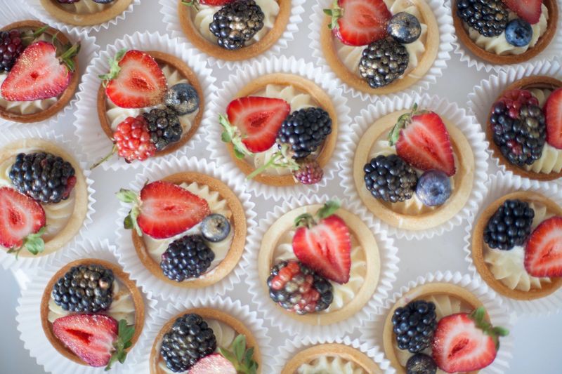 Tartellette assortite ai frutti di bosco in pirottini di carta, guarnite con fragole, more e mirtilli