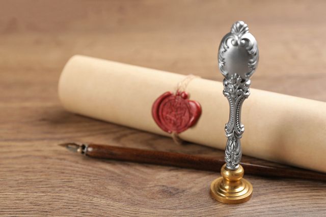 A scroll of paper with a wax seal and a pen on a wooden table.