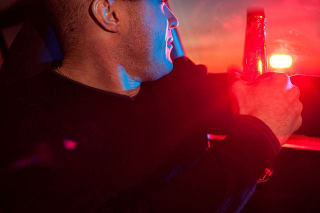 A man is holding a bottle of beer while driving a car.
