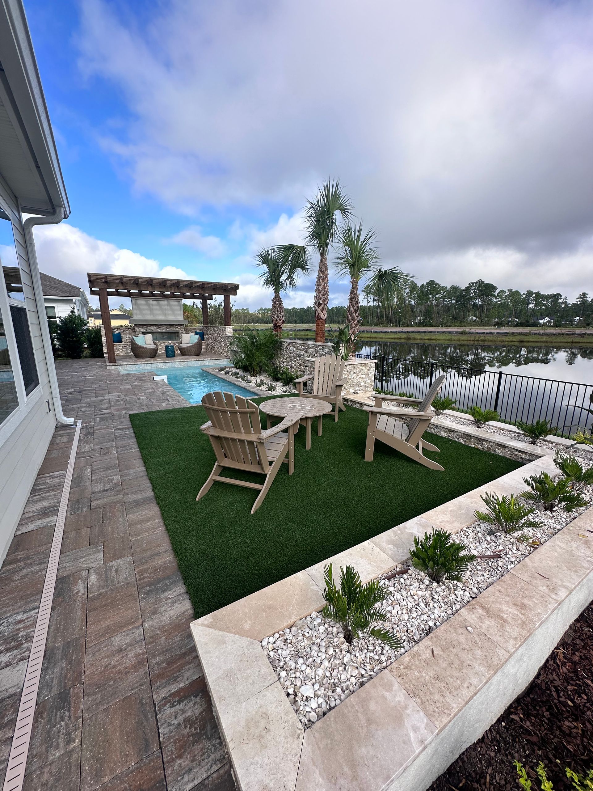 Backyard patio with pool, seating, and lake view under a partly cloudy sky.
