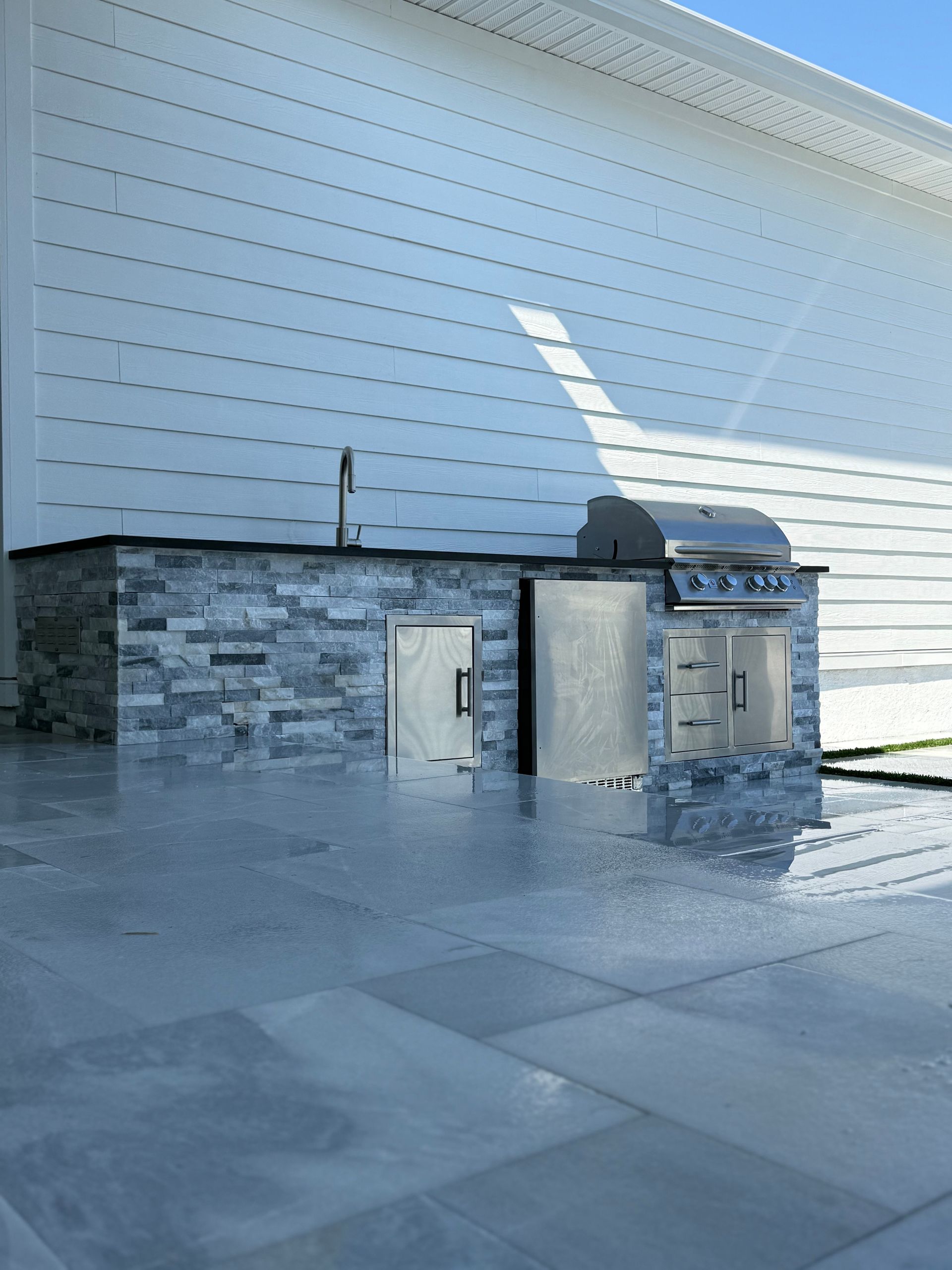 Outdoor kitchen with blue tiled facade and stainless steel grill.