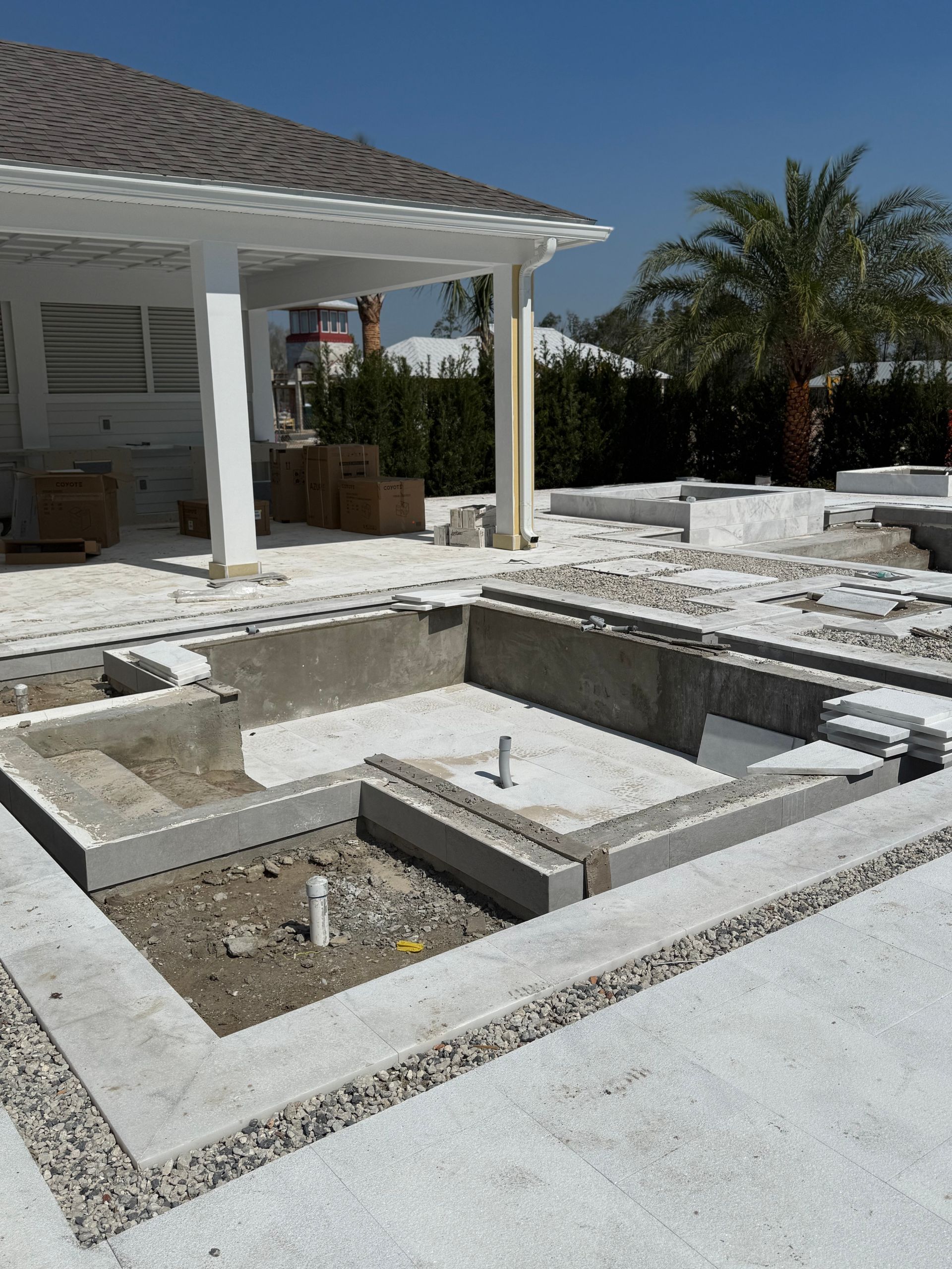 Pool under construction with concrete shell, steps, and surrounding stone, beside a cabana, outside.