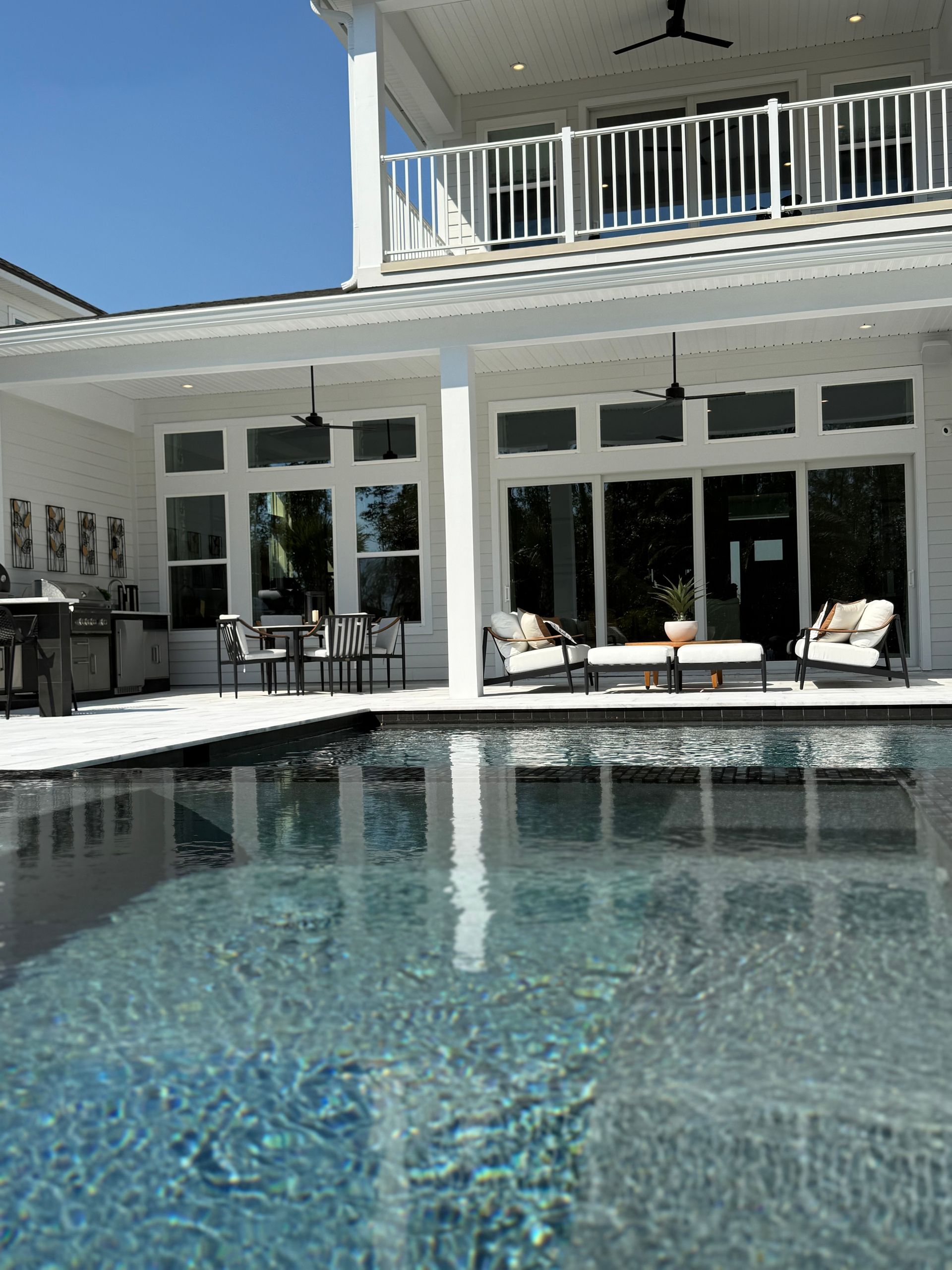 Poolside view of a white house with a balcony; reflecting in a dark blue pool.