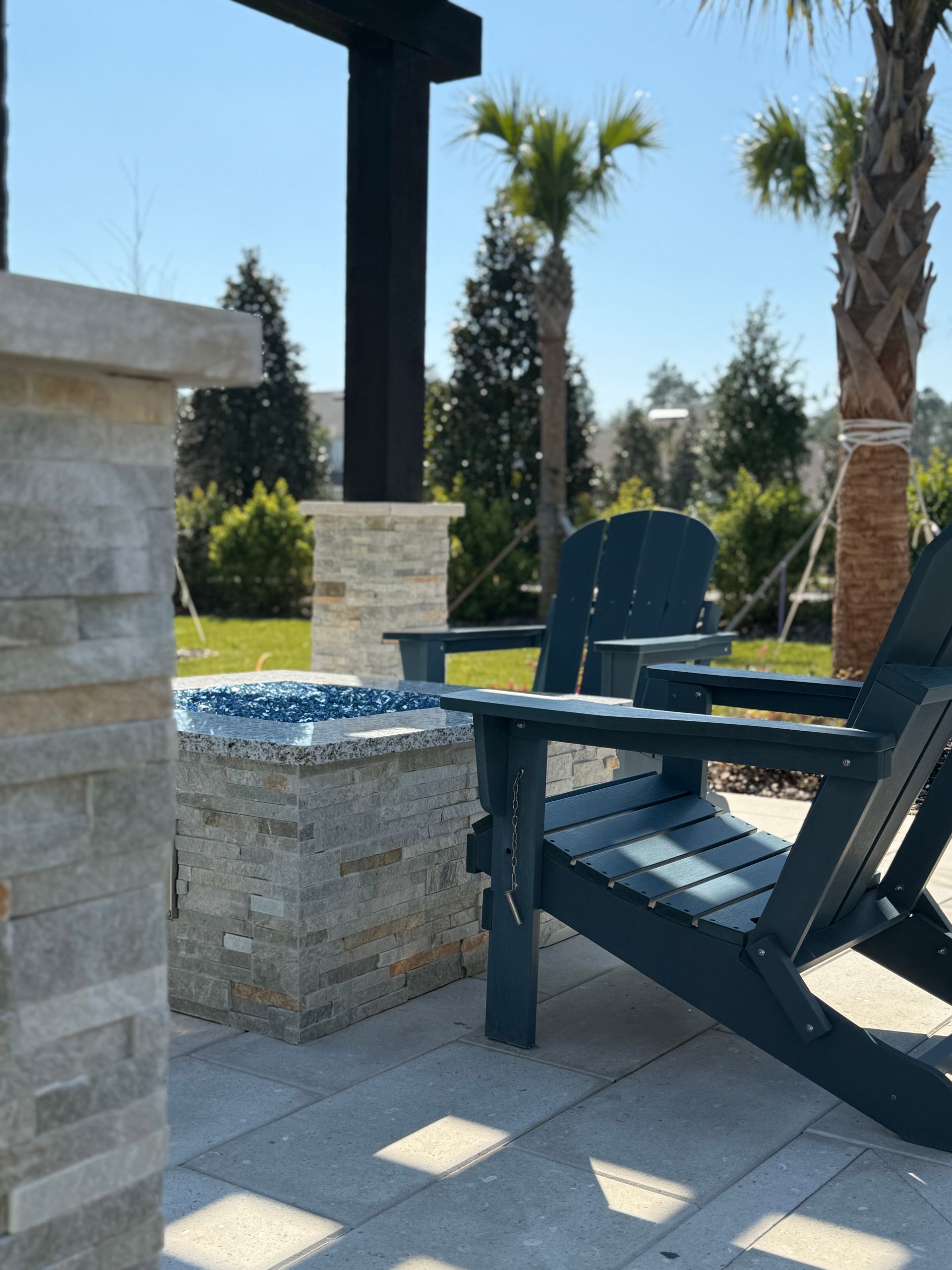 Fire pit with blue chairs in a backyard on a sunny day.