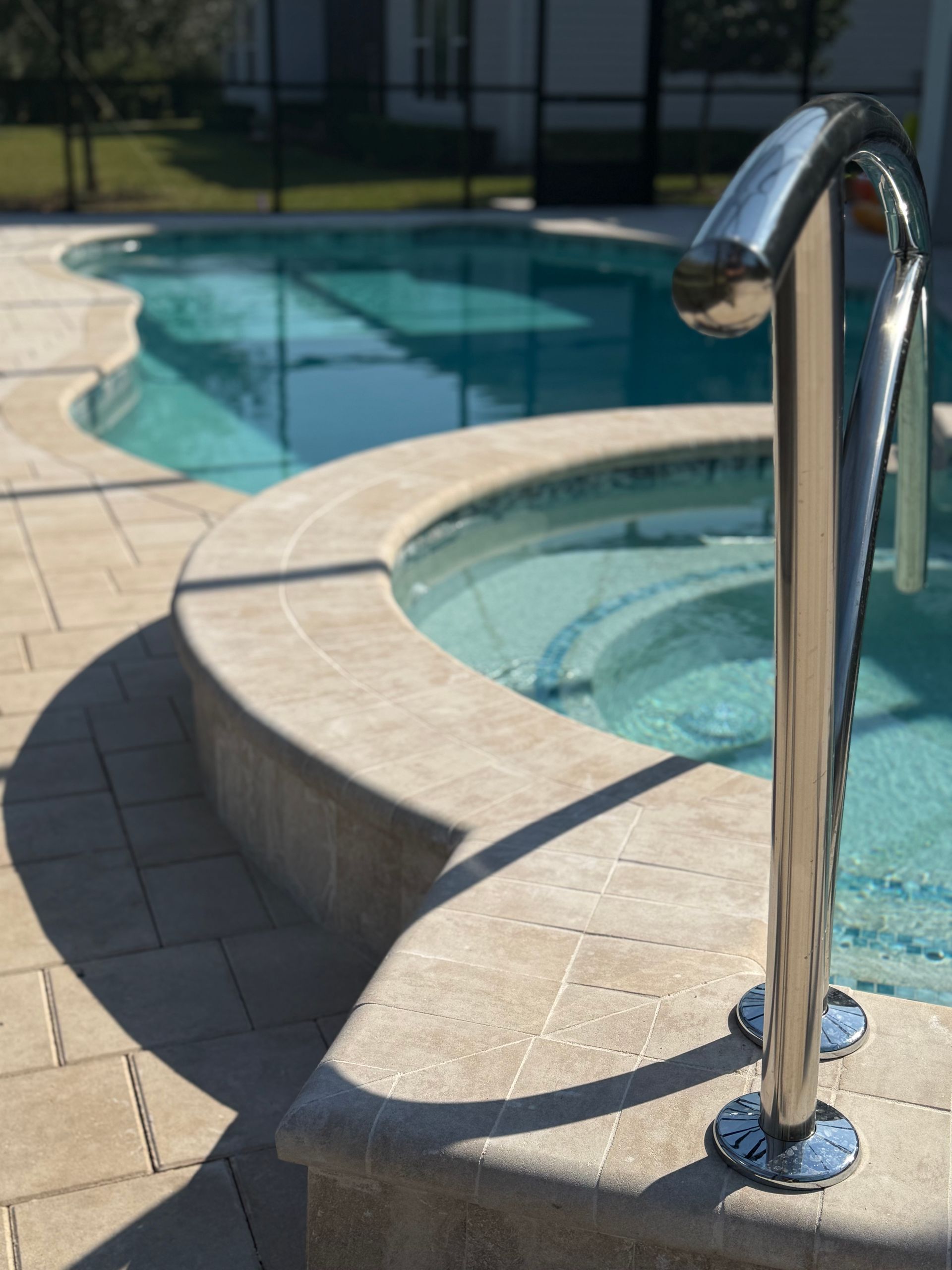 Pool and hot tub with stainless steel handrail, light-colored stone surround.