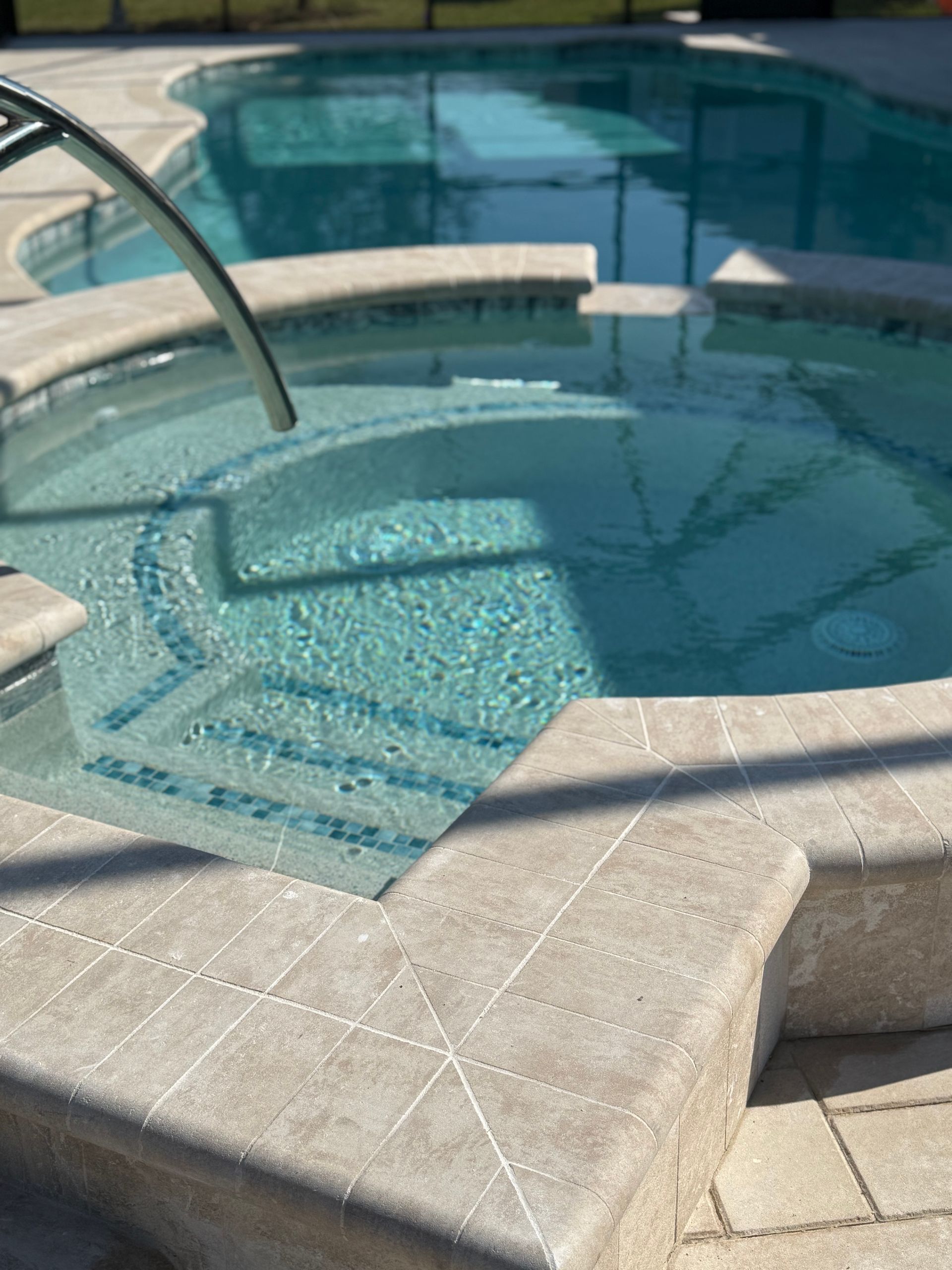 A close-up of a spa with blue-tiled steps, surrounded by light-colored paving and part of a swimming pool.
