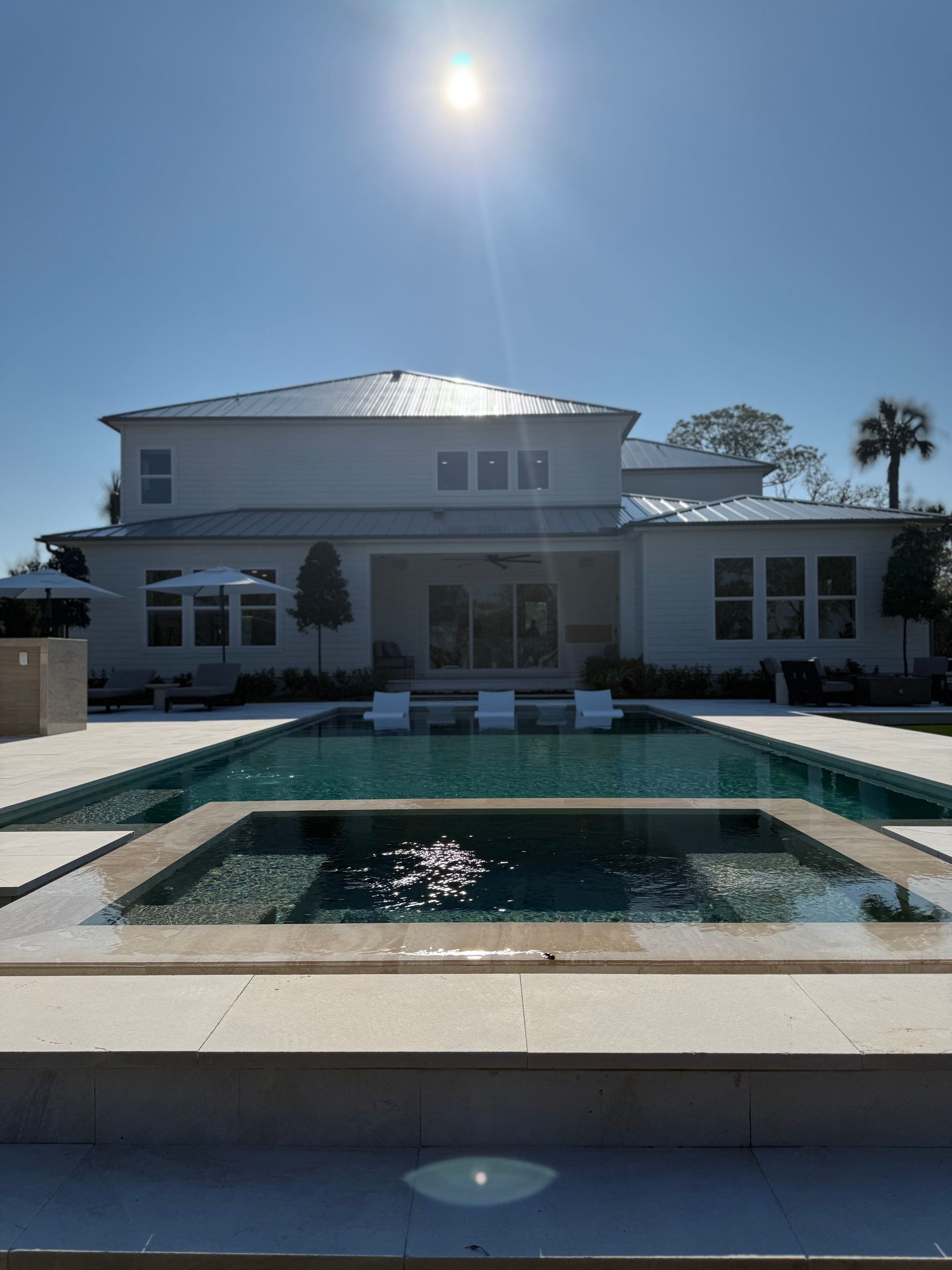 A large, light-colored house with a pool and spa on a sunny day.