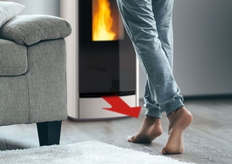 Barfußschritte auf einen Kamin neben einem grauen Sofa zu, ein roter Pfeil zeigt auf den Boden.