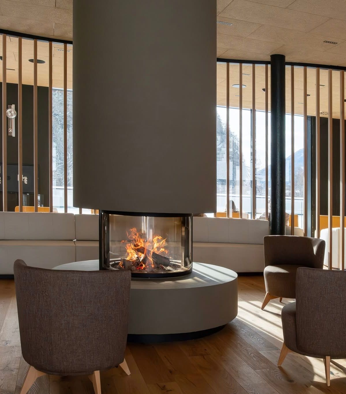 Modernes Wohnzimmer mit rundem Kamin, braunen Sesseln und bodentiefen Fenstern mit Bergblick