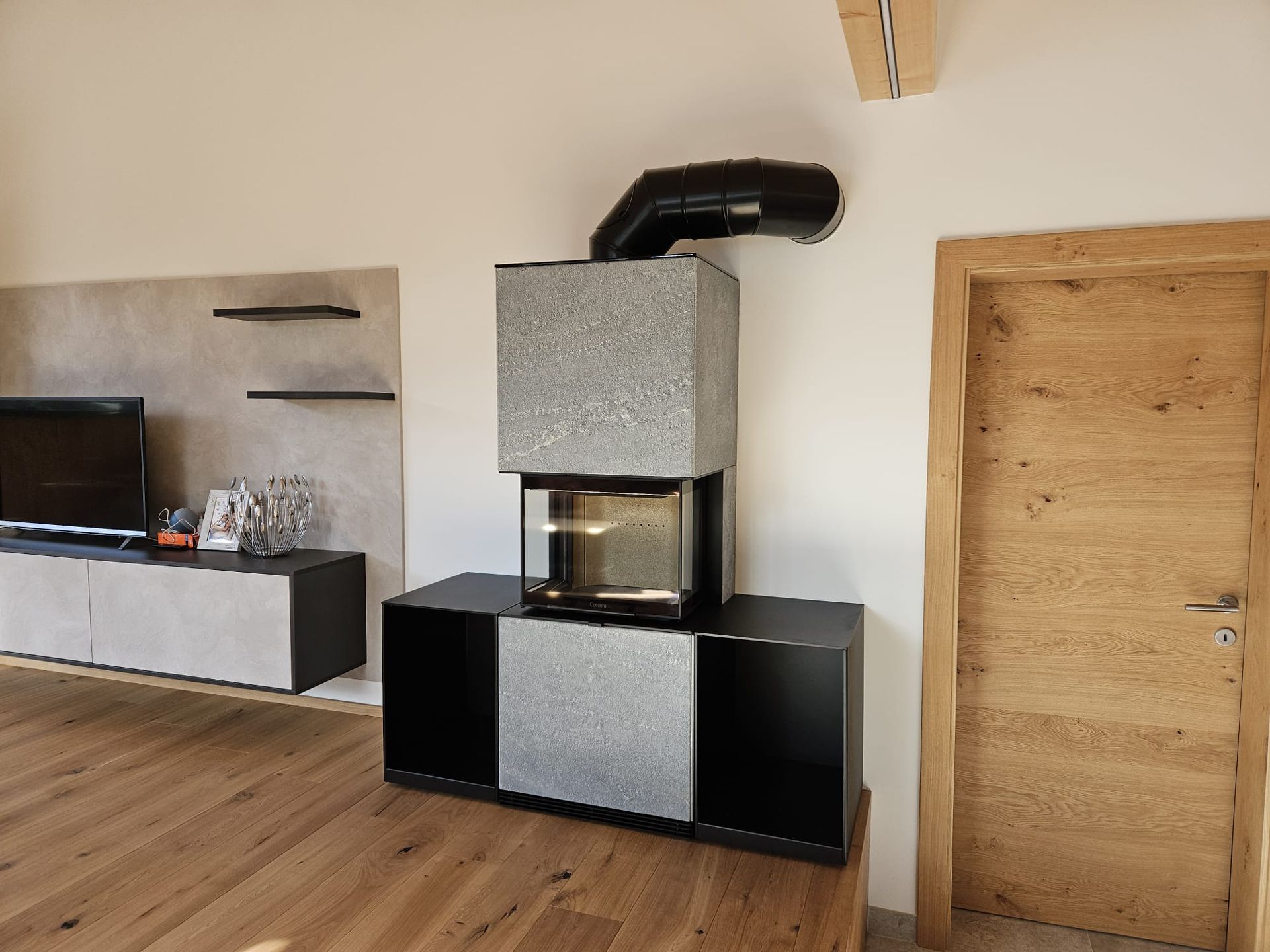 Modernes Wohnzimmer mit schwarz-grauem Kamin und Holzboden sowie einem niedrigen Fernsehschrank auf der linken Seite.