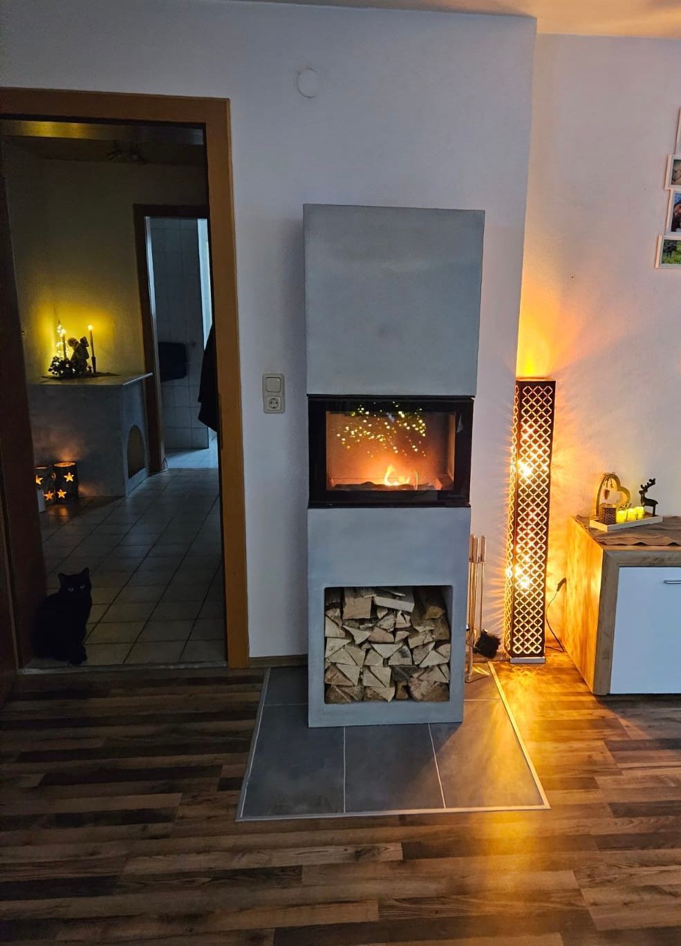 Modernes Wohnzimmer mit beleuchtetem Kamin, gestapelten Holzscheiten und Holzboden.