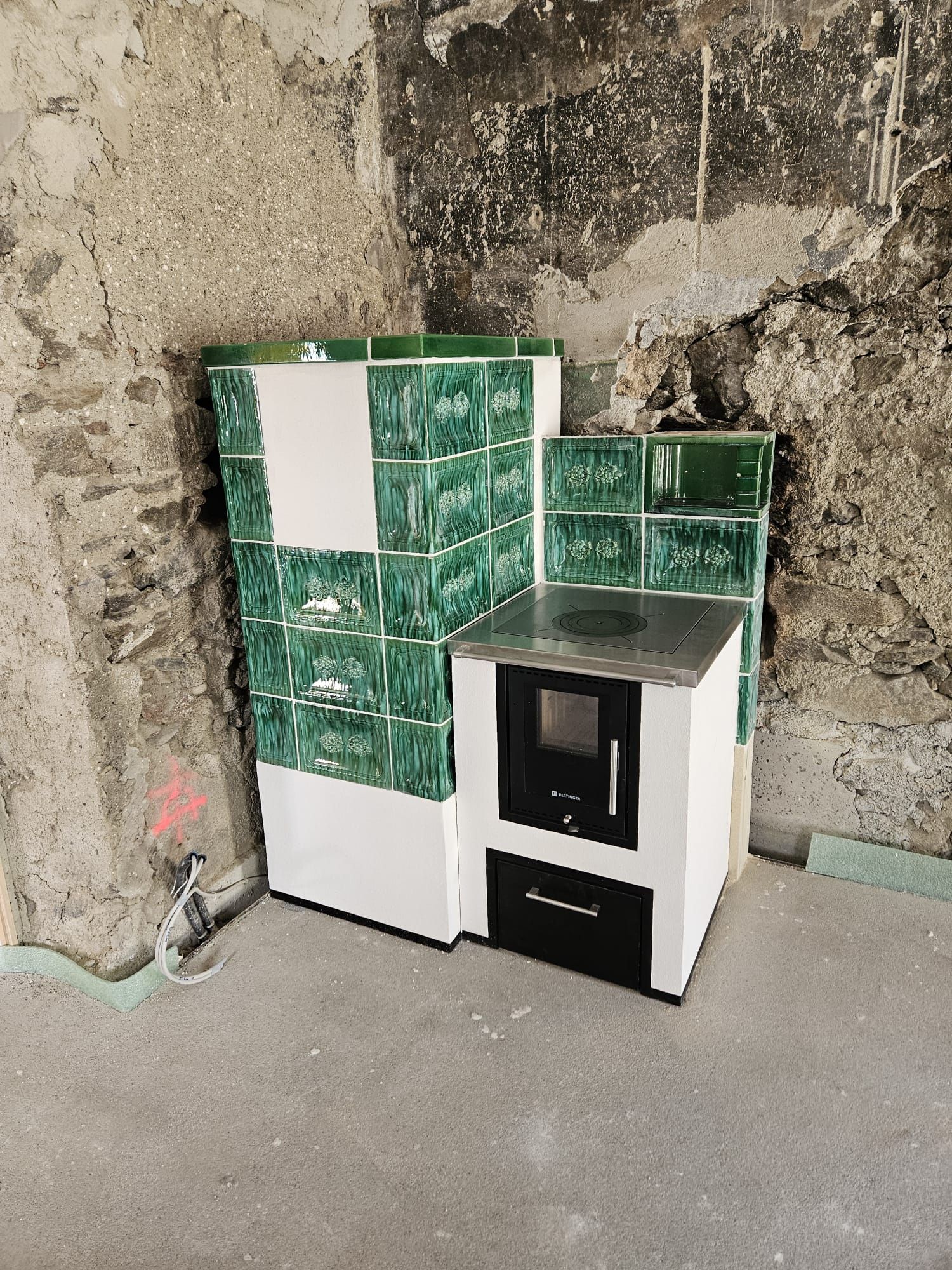 Kleiner, weiß-schwarzer Küchenschrank und Herd vor einer rauen, unfertigen Wand mit grünem Fliesenspiegel.