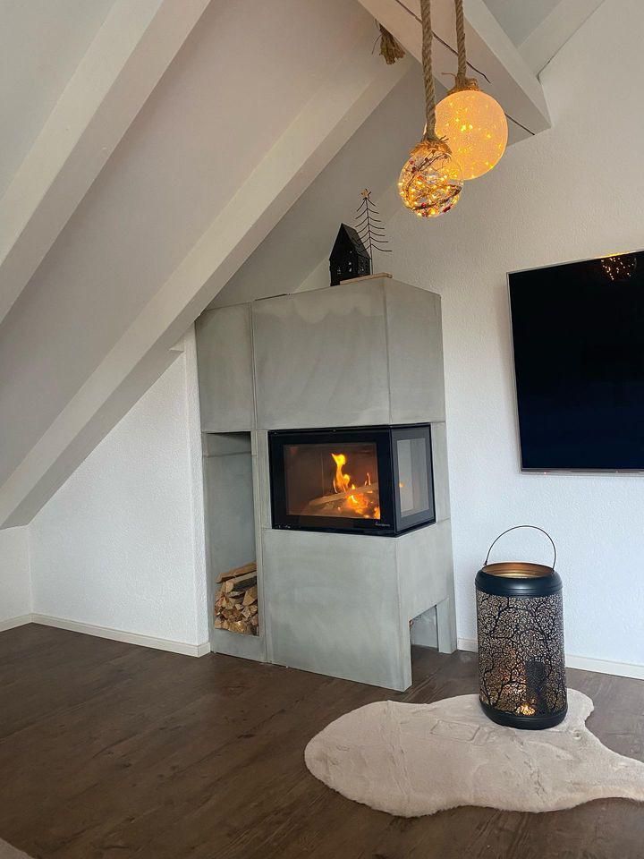 Modernes Wohnzimmer mit schrägen weißen Wänden, beleuchtetem Kamin, Pendelleuchten und an der Wand montiertem Fernseher