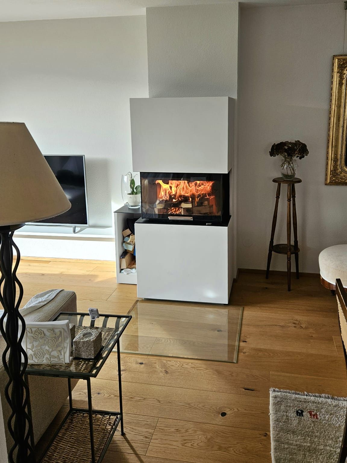 Modernes Wohnzimmer mit Kaminfeuer, Fernseher, Stehlampe und Holzboden