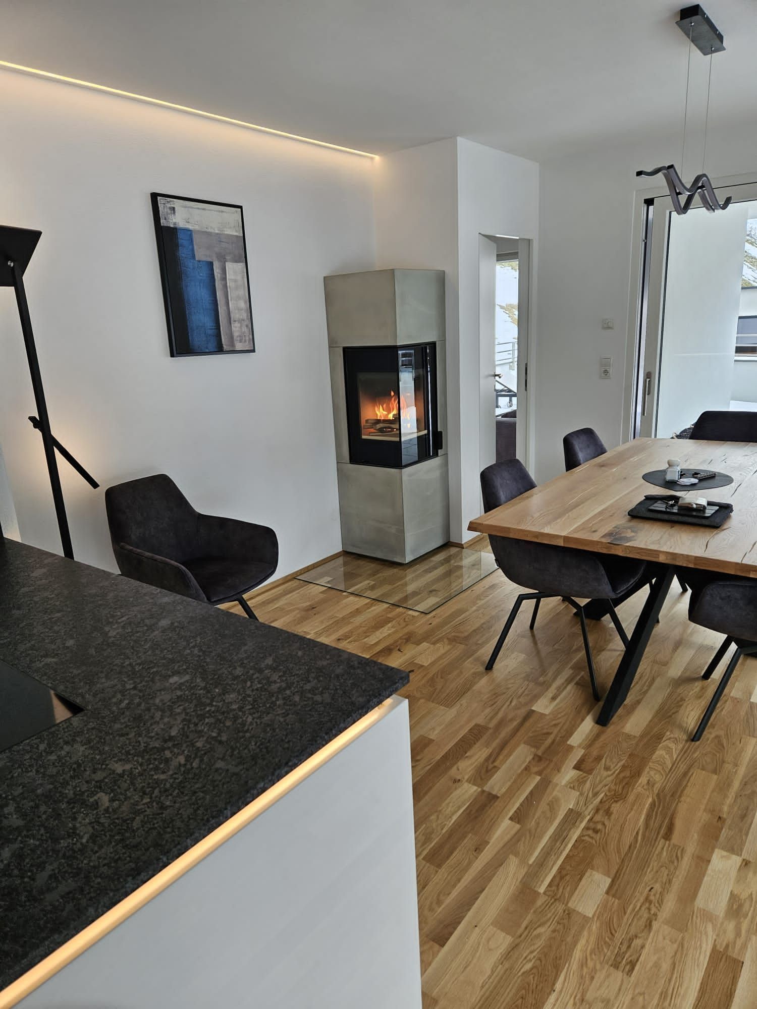 Modernes Wohnzimmer mit Eckkamin, schwarzem Sessel, Esstisch und Holzboden.