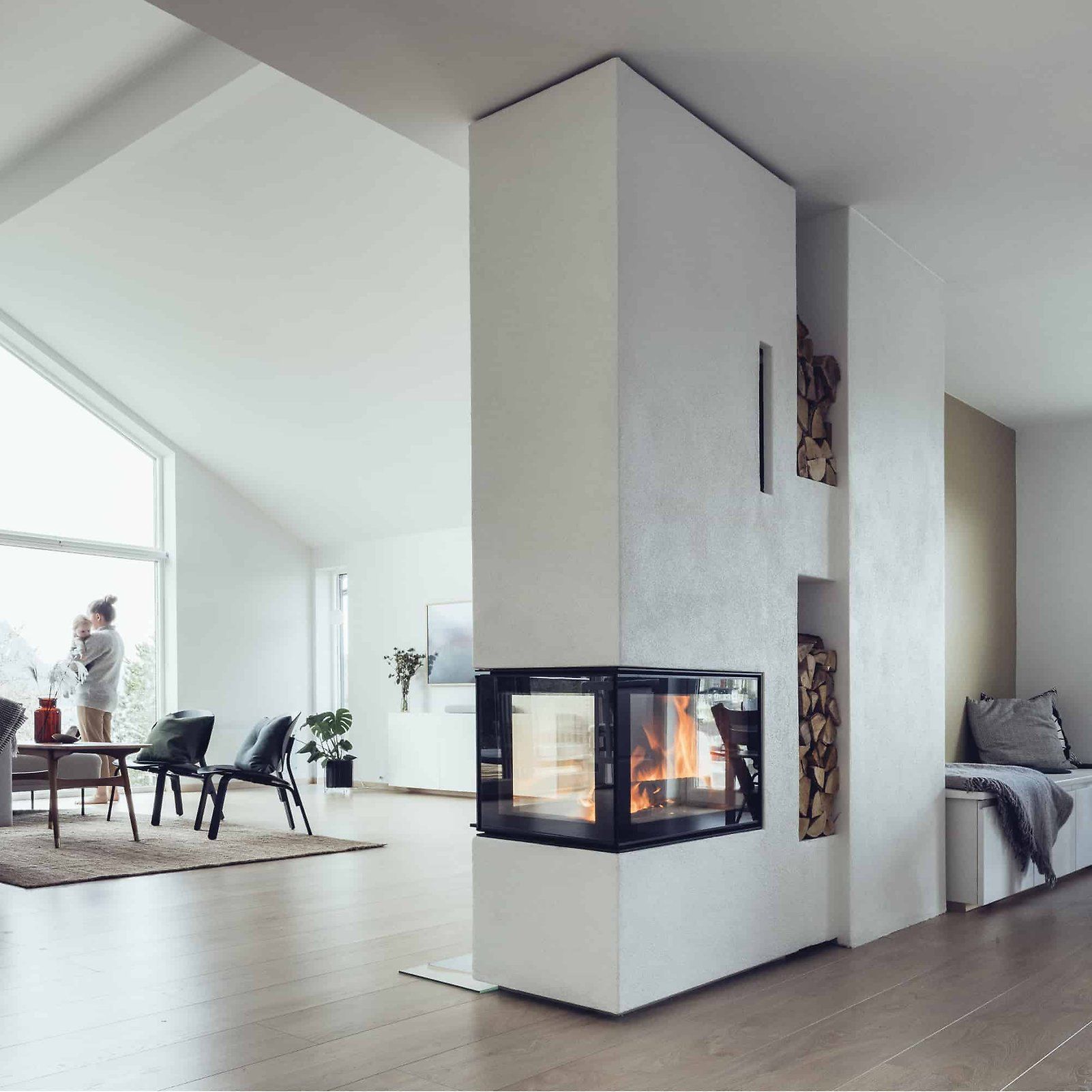 Modernes Wohnzimmer mit zentralem Glaskamin, weißen Wänden und einem Essbereich an großen Fenstern.