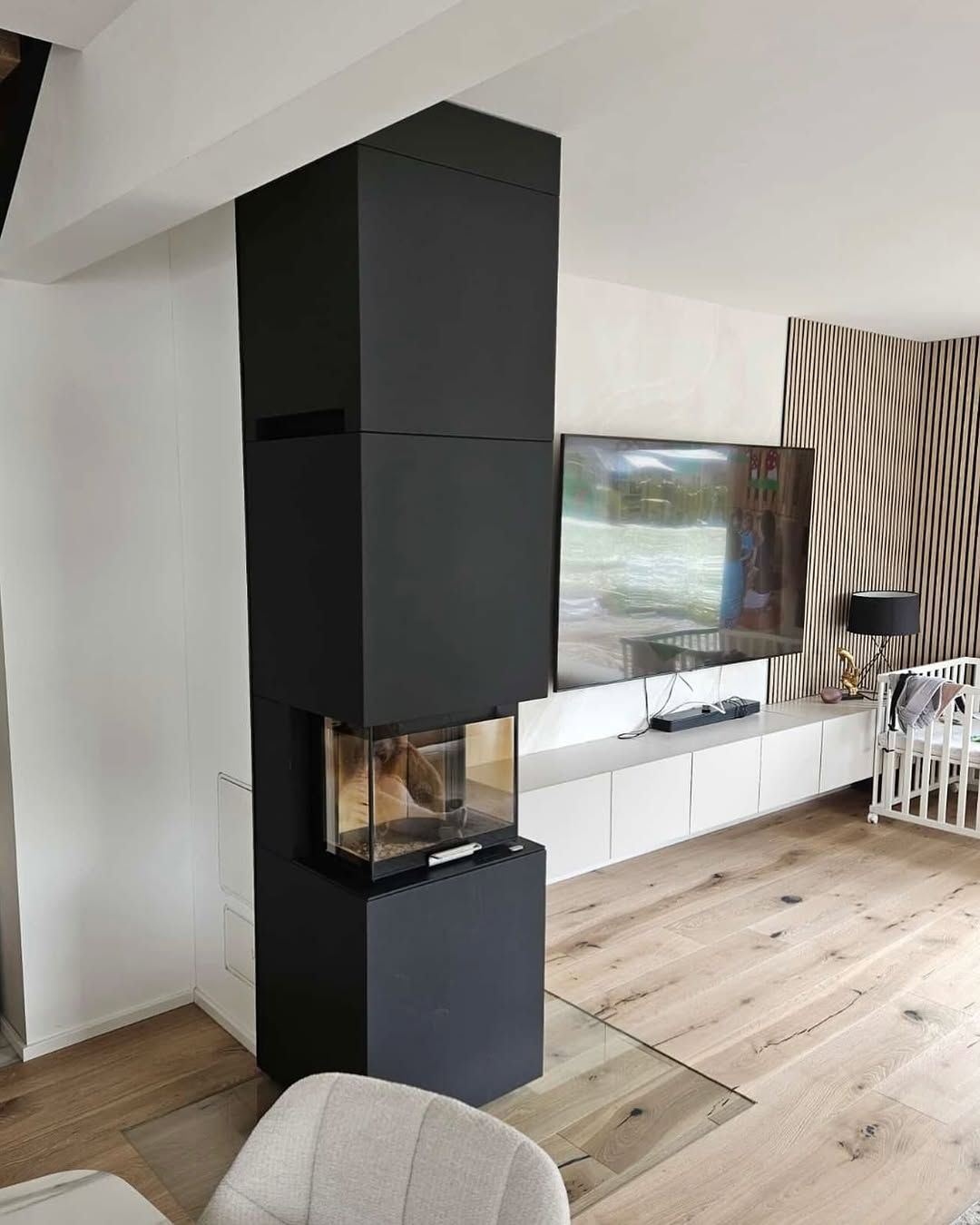 Modernes Wohnzimmer mit freistehendem schwarzen Kamin, Fernseher, weißen Schränken und geschwungenen Vorhängen.