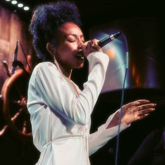 A man in a white shirt and brown pants is holding a tie over his shoulder