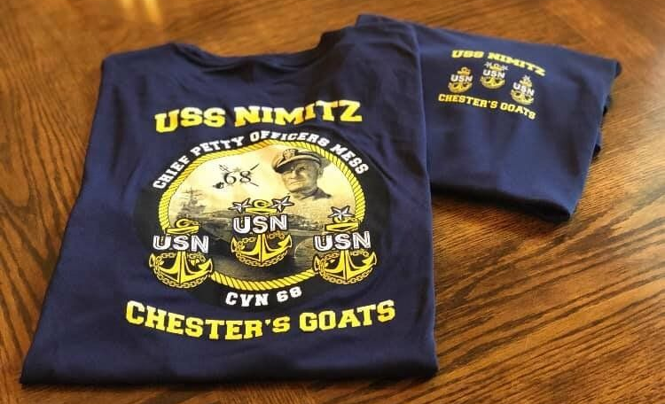 Navy T-shirt with yellow USS NIMITZ and “CHESTER’S GOATS” graphics, folded on a wooden table