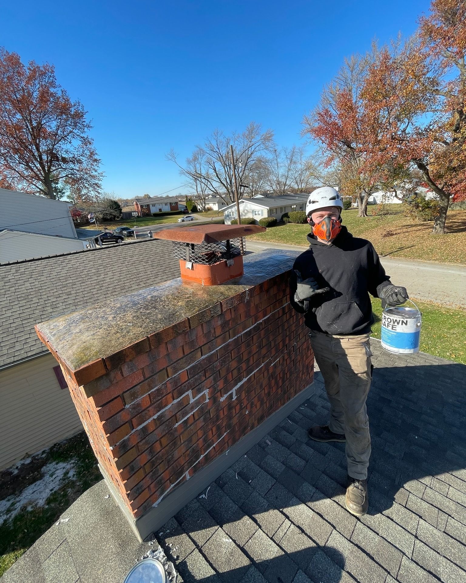 A man is standing on top of a brick chimney holding a bucket of paint.