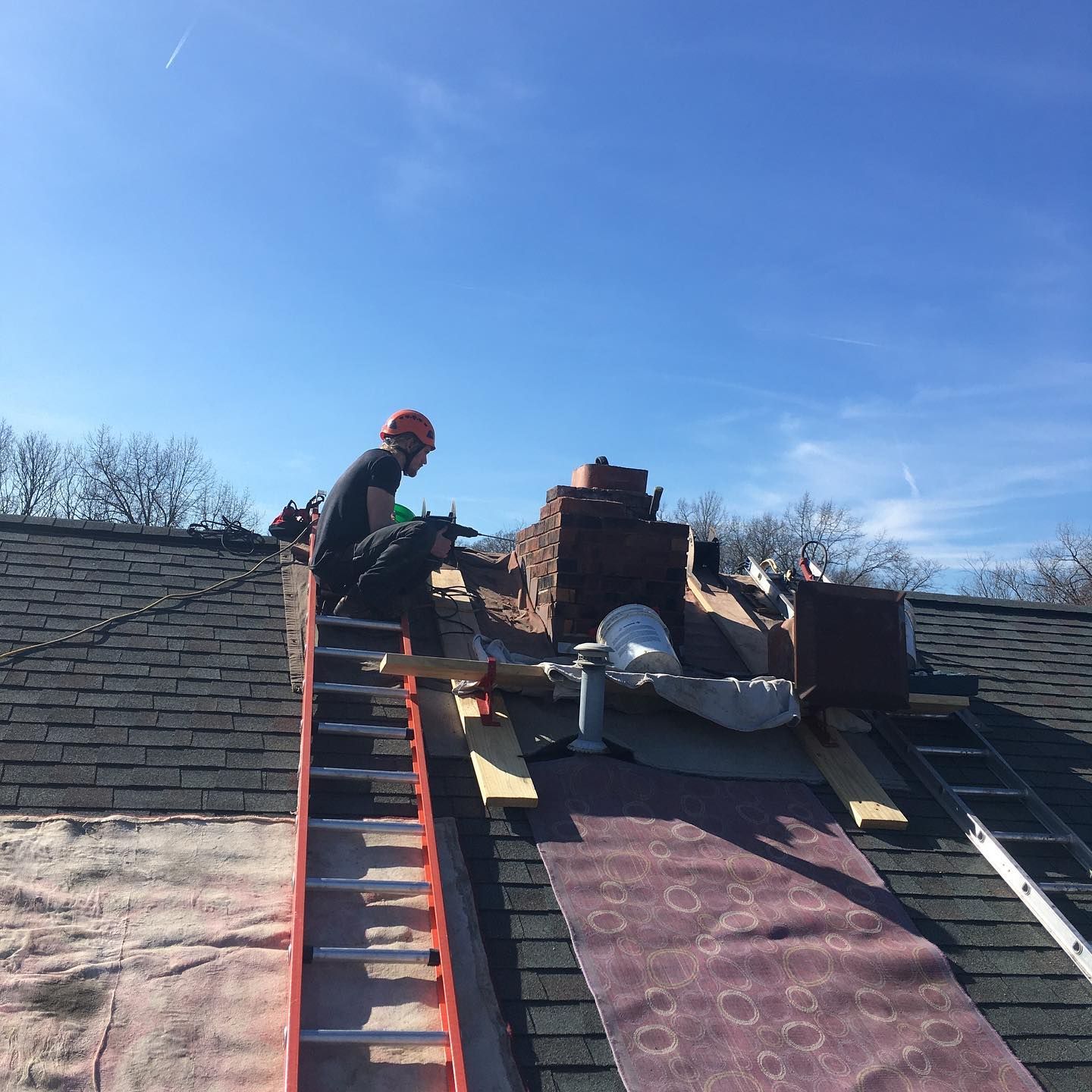 A man is sitting on top of a roof with a ladder.