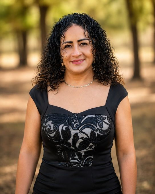 A woman standing with trees in the background.