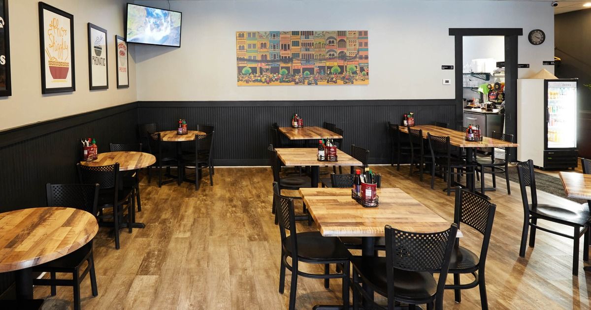 Empty café dining room with wooden tables, black chairs, and wall art on gray walls