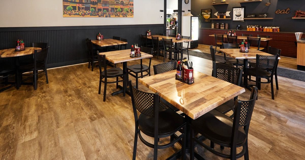 Empty restaurant dining room with wooden tables, black chairs, and warm lighting