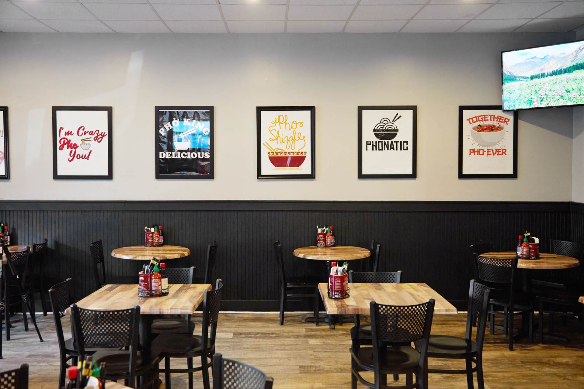 Empty casual dining area with wooden tables, black chairs, and framed posters on a gray wall.