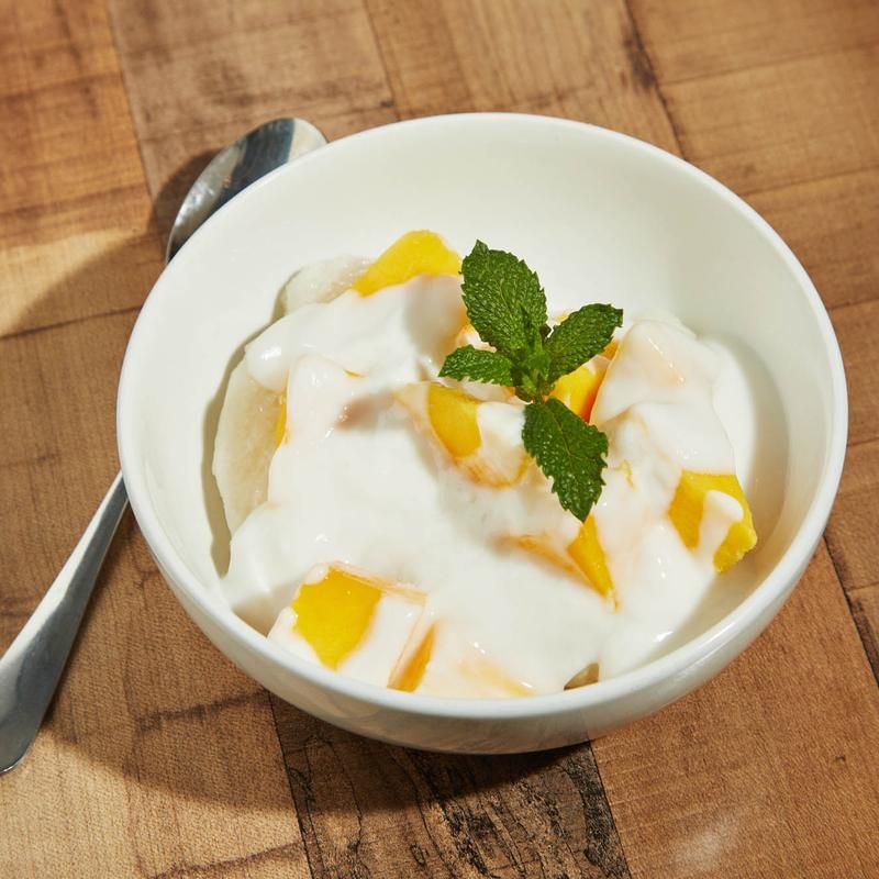 White yogurt dessert with mango pieces and mint garnish in a bowl on a wooden table