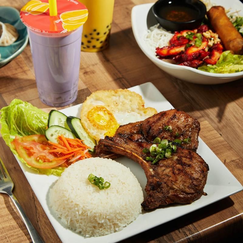 Rice plate with grilled steak, egg, salad, and drink on a wooden table